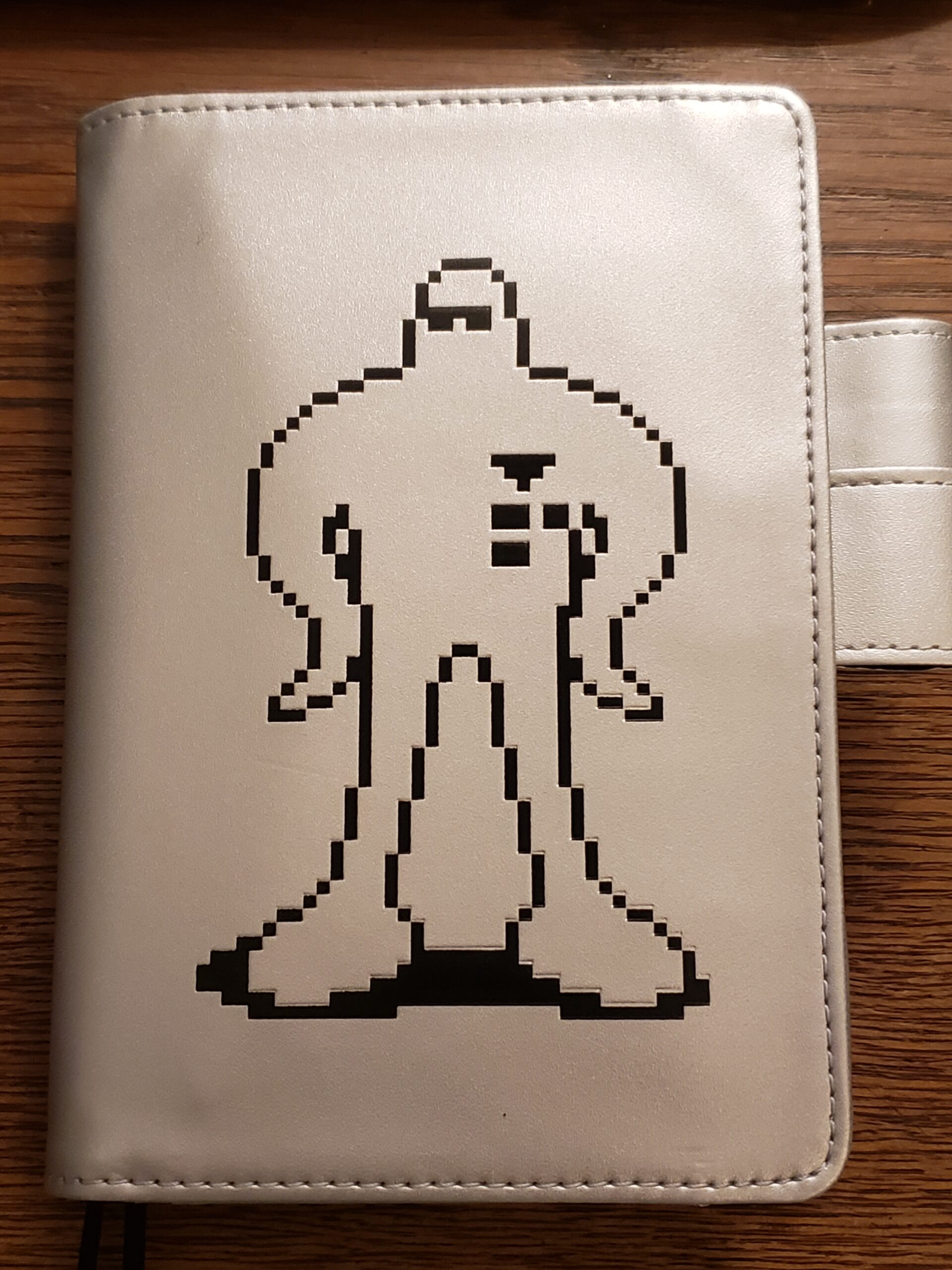 Silver Notebook With a Pixel Art Alien Figure Known as a Starman from Nintendo's Earthbound